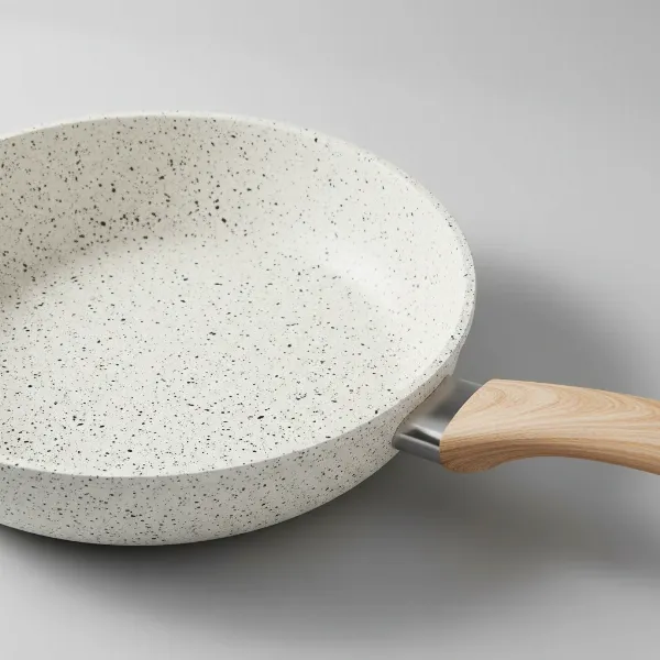 A close-up of the Carote white granite non-stick frying pan, highlighting its speckled surface and elegant design with a wooden handle.